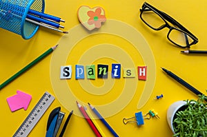 SPANISH made with carved letters on yellow desk with office or school supplies, stationery. Concept of Spanish language