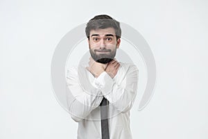 Spanish man with beard and white shirt holding hands by the throat on a gray background