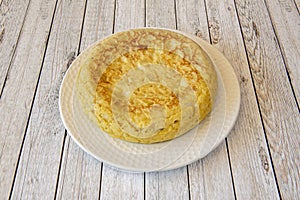 Spanish omelette with potatoes and eggs with a considerable thickness on a white plate and a light wood table