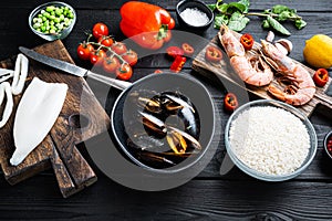 Spanish paella ingredients with rice, prawns, cuttlefish and mussel on black wooden table