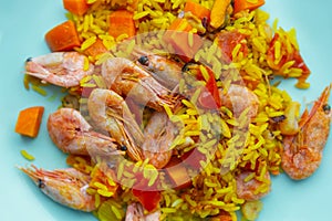 Spanish paella with shrimps,calamari,turmeric spice,red tomatoes & wild yellow rice served on plate.Overhead shot of delicious