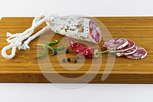 Spanish salami also sliced with dried red chili pepper and black pepper and rosemary on a wooden board