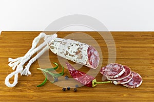 Spanish salami also sliced with dried red chili pepper and black pepper and rosemary on a wooden board