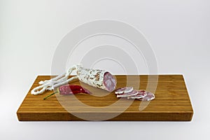 Spanish salami also sliced with dried red chili pepper on a wooden board with white background.