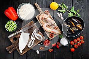 Spanish seafood paella ingredients, rice,prawns, mussels, peas on  black wooden background, flat lay