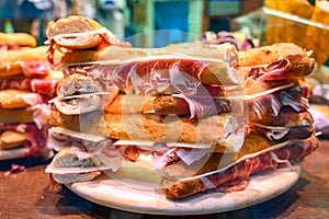 Spanish street food, fresh baked baguette bread with sliced iberian cured ham jamon, bocadillo