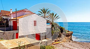 Spanish-style white house with red shutters and a roof against the backdrop of palm trees and the sea