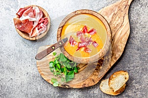 Spanish tomato soup Salmorejo served in olive wooden bowl with ham jamon serrano on stone background. Top view