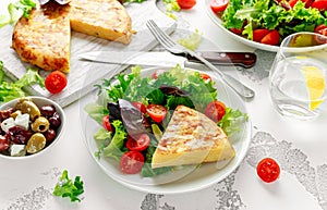 Spanish tortilla, omelette with potato, onion, vegetables, tomatoes, olives and herbs in a white plate. breakfast