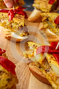 Spanish tortilla pintxos on a wooden board. Han putting the toothpick in the pintxo.