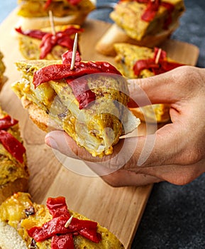 Spanish tortilla pintxos  on a wooden board. Male hand holding one pintxo.