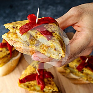 Spanish tortilla pintxos  on a wooden board. Male hand holding one pintxo.