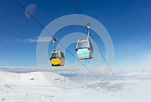 Two cable car cabins high above snowy mountains with the moon in the sky.