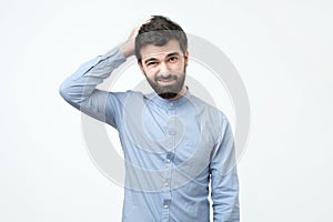 Spanish young man with black beard thinking, scratching his head.