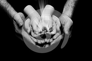 Spark of hope in a child hands wh holding by parents handson dark background. The light of faith