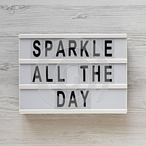 `Sparkle all the day` words on a modern board on a white wooden background, top view. Overhead, from above, flat lay. Close-up