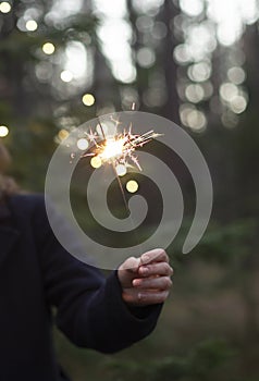 Sparkler firework in women`s hand in forest. Christmas holidays celebration concept