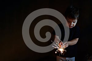 A sparkler is in the hands of a happy boy. Dark background.