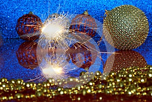 Sparklers, Christmas toys and golden tinsel on a blue background and a mirror surface. New Year`s magic