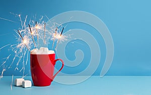 Sparklers in red cup with marshmallow and hot cocoa on blue