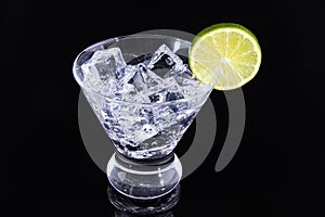 Sparkling beverage in a martini glass with a lime slice on a black background
