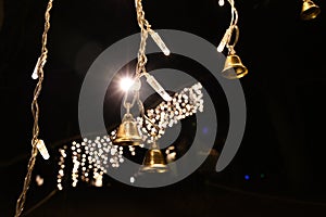 Sparkling bright light of Christmas decorations with shining lights garlands and small shiny metal bells on black background.