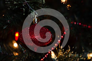 Sparkling bright red Christmas ornament. Twinkle light with ornament and garland on a Christmas tree.