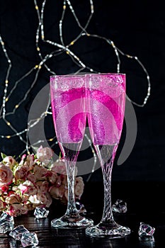 Sparkling brilliant raspberry drink. Champagne in two glasses stands on a wooden table with ice. For flowers and a garland