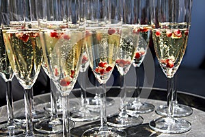 Sparkling champagne flutes on tray with pomegranate seeds.