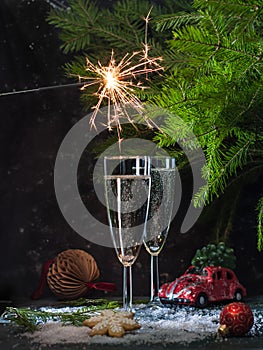 sparkling champagne on New Year's Eve in a tall glass with sparklers and fir branches on a dark background