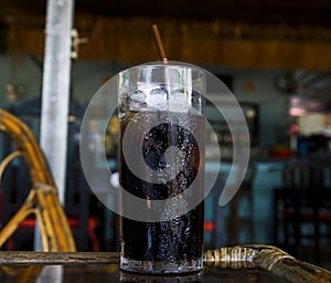Sparkling drink with ice in glass. Cool beverage in hot summer day. Coke in glass with straw