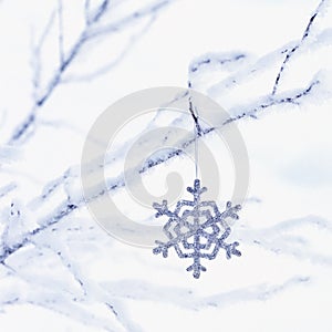 Sparkling glitter snowflake Christmas ornament decoration hanging from frosty branches with white snow background. Winter holiday