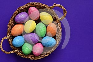 Sparkling glittering colored candy Easter eggs in a wicker basket, top view