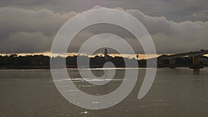 Sparkling light of the sunset on the Mekong river and cloudy sky over an old lookout tower by the riverside in the background