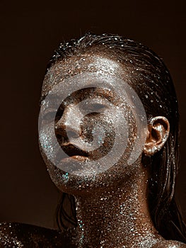 Sparkling silver body art on female face, sensual young girl with wet hair and glitter on skin, close up portrait