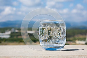 Sparkling water glass on a stone parapet with a mountain view. Cool glass of mineral water. Mountain mineral water