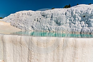 The sparkling white terraces of shallow limestone pools filled with azure blue water at  Pamukkale, Turkey