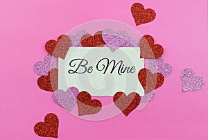 Sparkly pink and red hearts surround a parchment paper tage on a bright pink background for Valentine`s Day in February. Message