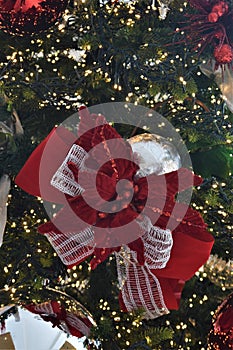 Sparkly silver ornament with red and white ribbon hanging from greenery and surrounded by lights.