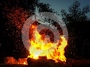 Sparks bounce off from a bonfire at night after a log thrown into it