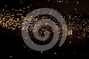 Sparks in dark. Flow of sparks from metal processing. Lights on black background. Work in workshop. Grinding steel. Many small