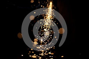 Sparks in dark. Flow of sparks from metal processing. Lights on black background. Work in workshop. Grinding steel. Many small