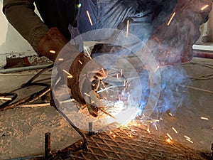 Sparks from a welding torch during the work of the welder. The master solders a metal rod with a tool. Worker cuts reinforced