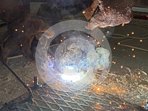 Sparks from a welding torch during the work of the welder. The master solders a metal rod with a tool. Worker cuts reinforced