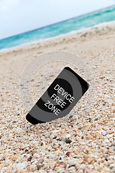 Spartphone with text device free zone written in its screen placed in the sand of a beach