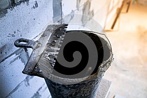 A spatula-comb in an adhesive solution lies on a bucket at a construction site close-up. Facade notched trowel for uniform