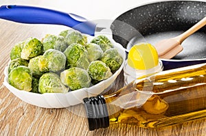Spatula in frying pan, frozen broccoli in bowl, salt, bottle of vegetable oil on table
