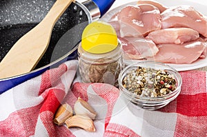 Spatula in frying pan, white plate with pieces of chicken meat, pepper, bowl with condiment, garlic on napkin