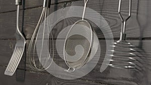 Spatula, whisk, masher and strainer hanging against rustic wooden grey wall in restaurant or home kitchen. Kitchen