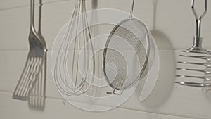 Spatula, whisk, masher and strainer hanging against rustic wooden white wall in restaurant or home kitchen. Kitchen